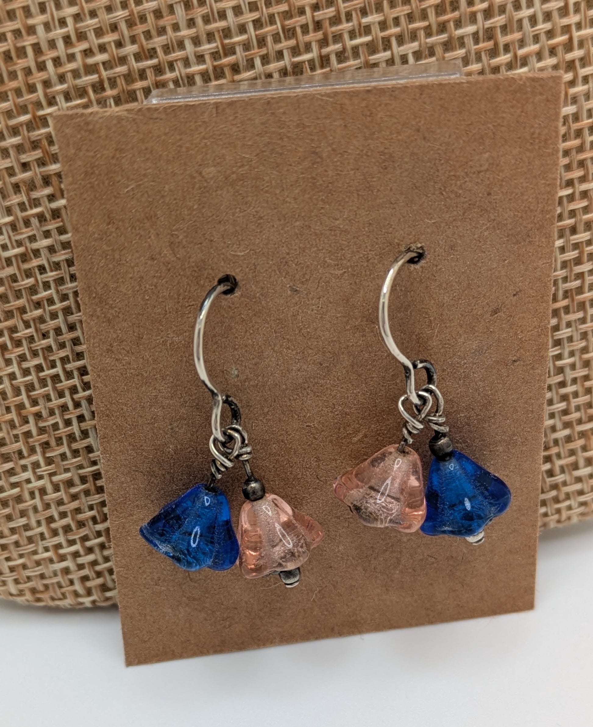 Pair of earrings with blue and pink glass drops on a brown card.