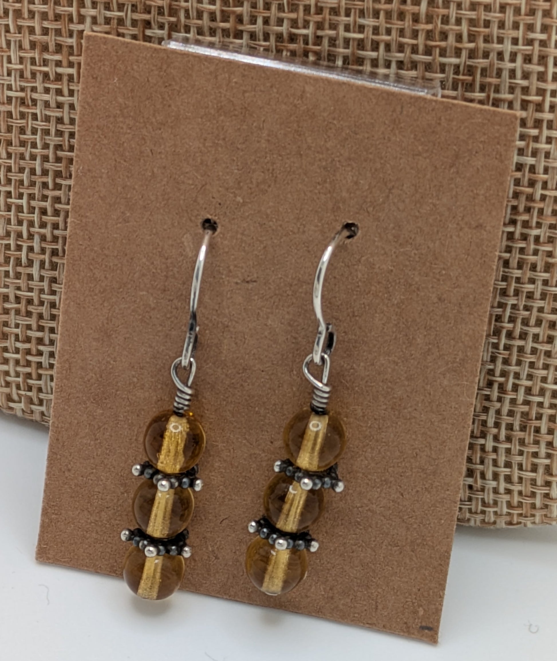 Pair of beaded earrings on a brown card with a woven background